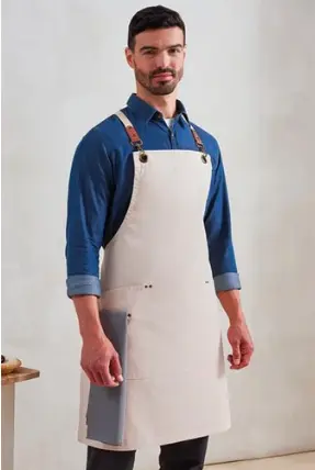 Man wearing an off-white chef apron with leather straps over a blue shirt